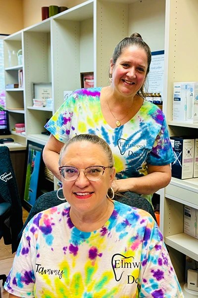 Dentist and staff member in tie-dye scrubs smiling in office