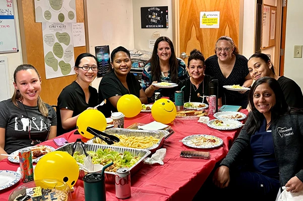 Staff enjoying potluck meal with yellow balloons and festive table