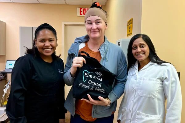 Team posing with &ldquo;Elmwood Pediatric Dental&rdquo; tote bag at event