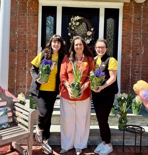 Three team members posing with potted plants outside clinic entrance