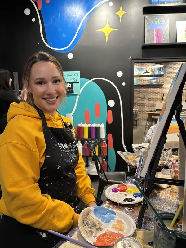 Staff member in yellow hoodie painting at easel in studio