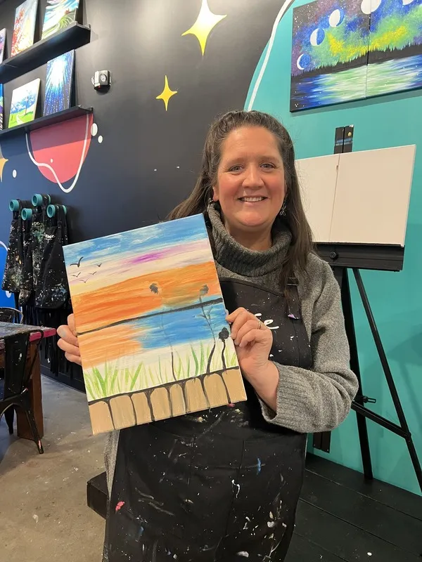 Woman proudly holding her painted landscape artwork